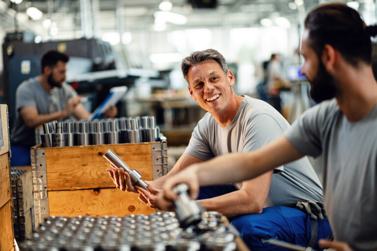 Two happy steel workers preparing manufacture products for the distribution and communicating in industrial facility. Focus is on mid adult worker.